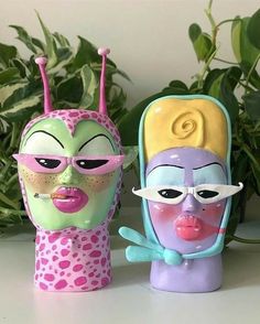 two plastic toys with faces painted on them sitting next to each other in front of plants