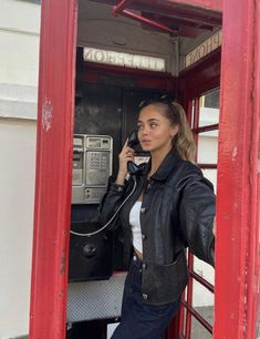 a woman standing in a red phone booth