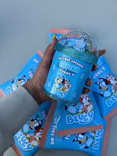 a person holding up a cup filled with gummy bears on top of blue packets