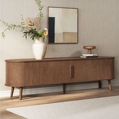 a vase with flowers sitting on top of a wooden cabinet next to a painting and rug