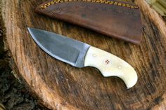 a knife sitting on top of a piece of wood next to a knife holder with a leather sheath