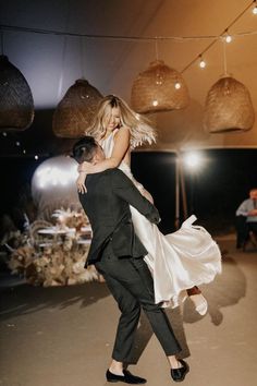 a man and woman are dancing together in the middle of a room with lights hanging from the ceiling