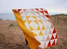 a person holding up a quilt on the beach