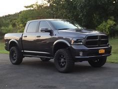 a large gray truck parked on top of a parking lot next to some green trees