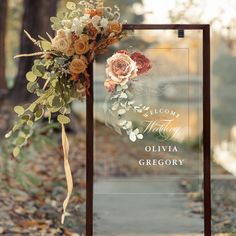 a welcome sign with flowers and greenery on the front is displayed in an autumn setting