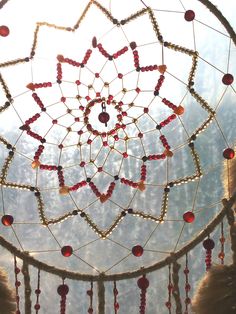 a dream catcher with red beads hanging from it's sides in front of trees