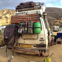 an old truck is parked in the dirt with many items on it's back