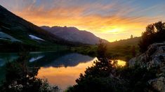 the sun is setting over a mountain lake