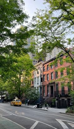 a yellow taxi driving down a street next to tall buildings with trees on both sides