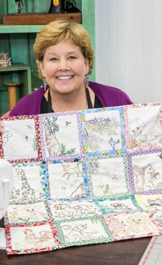 a woman sitting at a table holding up a quilt