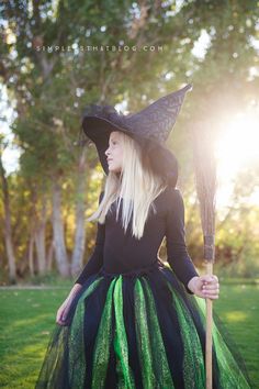 a woman in a witch costume holding a broom and wearing a black hat with green stripes