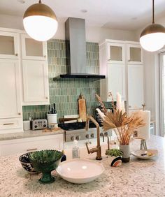 a kitchen with white cabinets and green tile backsplash, two hanging lights above the sink