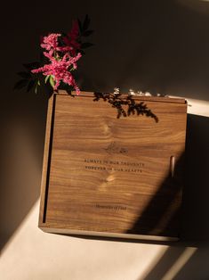 a wooden box with flowers in it sitting on a table next to a shadow cast wall