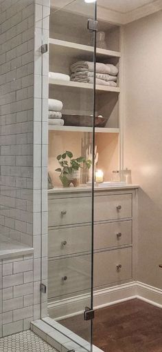 a bathroom with a glass shower door and white tile on the walls, along with wooden flooring