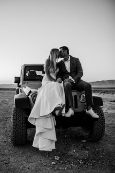 a bride and groom sitting on the back of a truck in front of an open field