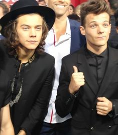 two men standing next to each other in front of a crowd wearing black suits and hats