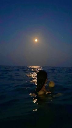 a woman swimming in the ocean at night with the moon above her head and water below