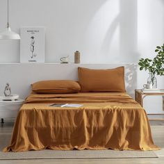 a bed with orange sheets and pillows in a white room next to a potted plant