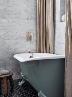 a bath tub sitting next to a wooden stool in a bathroom with marble tiles on the walls