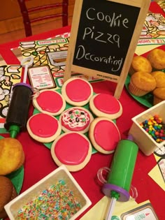 a table topped with cupcakes, donuts and sprinkles next to a sign that says cookie pizza decorating