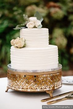 a white wedding cake sitting on top of a table next to gold utensils