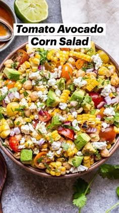 a bowl filled with corn salad and garnished with cilantro, avocado, feta cheese and lime