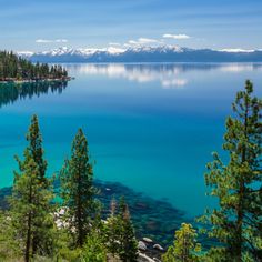 a lake surrounded by trees and snow capped mountains in the distance with clear blue water