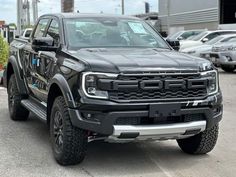 a large black truck parked in a parking lot next to other cars and trucks behind it