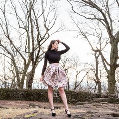 a woman standing on top of a rock covered ground wearing a skirt and black shirt