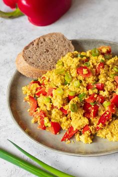 scrambled eggs with tomatoes and green onions on a silver plate next to bread, celery and red peppers