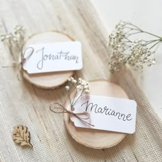 two place cards with names on them sitting on a wooden plate next to some flowers