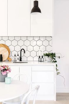 a white kitchen with hexagonal tile backsplash and black pendant lights over the sink