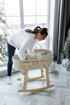 a woman bending over to look at a baby in a crib next to a window