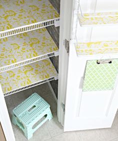 a white closet with yellow and green wallpaper next to a blue step stool on the floor