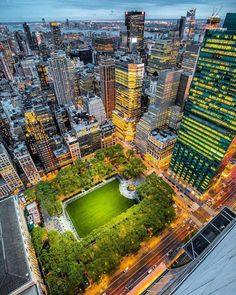 an aerial view of a city with lots of tall buildings and green grass in the middle