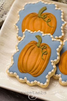 three decorated pumpkin cookies sitting on top of a white plate with blue border around the edges