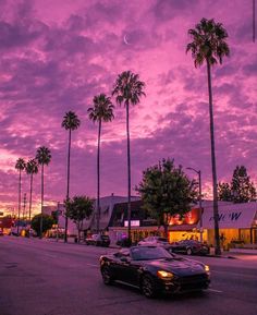 a car is driving down the street in front of palm trees and buildings at sunset