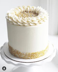 a cake with white frosting and gold sprinkles sitting on a plate