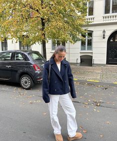 an older woman walking down the street in front of a tree with leaves on it