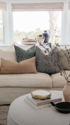 a living room filled with furniture and pillows on top of a white coffee table in front of a window