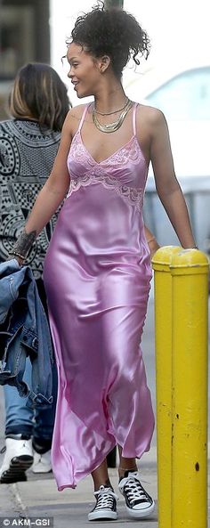 a woman in a pink dress walking down the street with her hand on her hip