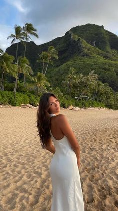 a woman standing on top of a sandy beach next to palm tree covered mountains in the background