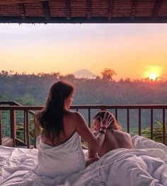 two women sitting on a bed looking at the sunset