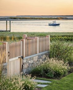 a boat is in the water behind a stone wall and wooden fence with grass on both sides