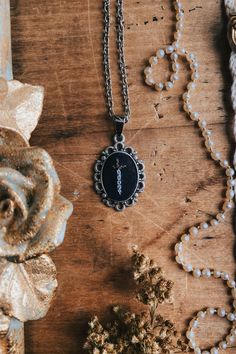 a necklace with the letter i on it sitting next to a flower and bead