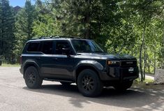 a black suv parked on the side of a road next to some rocks and trees