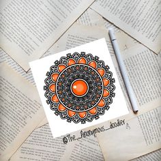 an orange and black design is on top of some old book pages with a pen next to it