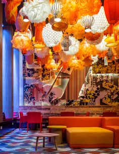 a room filled with lots of orange and white lights hanging from the ceiling next to red chairs