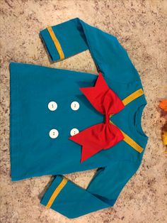 a child's blue shirt with a red bow on the front and buttons on the back