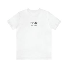 "Introducing our exceptional Bride t-shirt, the epitome of style and sophistication for your big day. Immerse yourself in unparalleled elegance with this meticulously crafted garment, meticulously designed to showcase your role as the Bride. Made from premium-quality materials, our t-shirt offers unmatched comfort and a flawless fit. The word \"Bride\" is intricately printed on the shirt, adding a touch of distinction to your wedding ensemble. With its exceptional craftsmanship and attention to White Bridal T-shirt With Short Sleeves, Custom Text Short Sleeve Tops For Wedding, White Fitted T-shirt For Bachelorette Party, Customizable Short Sleeve Wedding Tops, Customizable Short Sleeve Tops For Wedding, White Custom Text Top For Wedding, White Custom Text T-shirt For Weddings, White T-shirt For Bridal Shower Short Sleeve, White Short Sleeve T-shirt For Bridal Shower